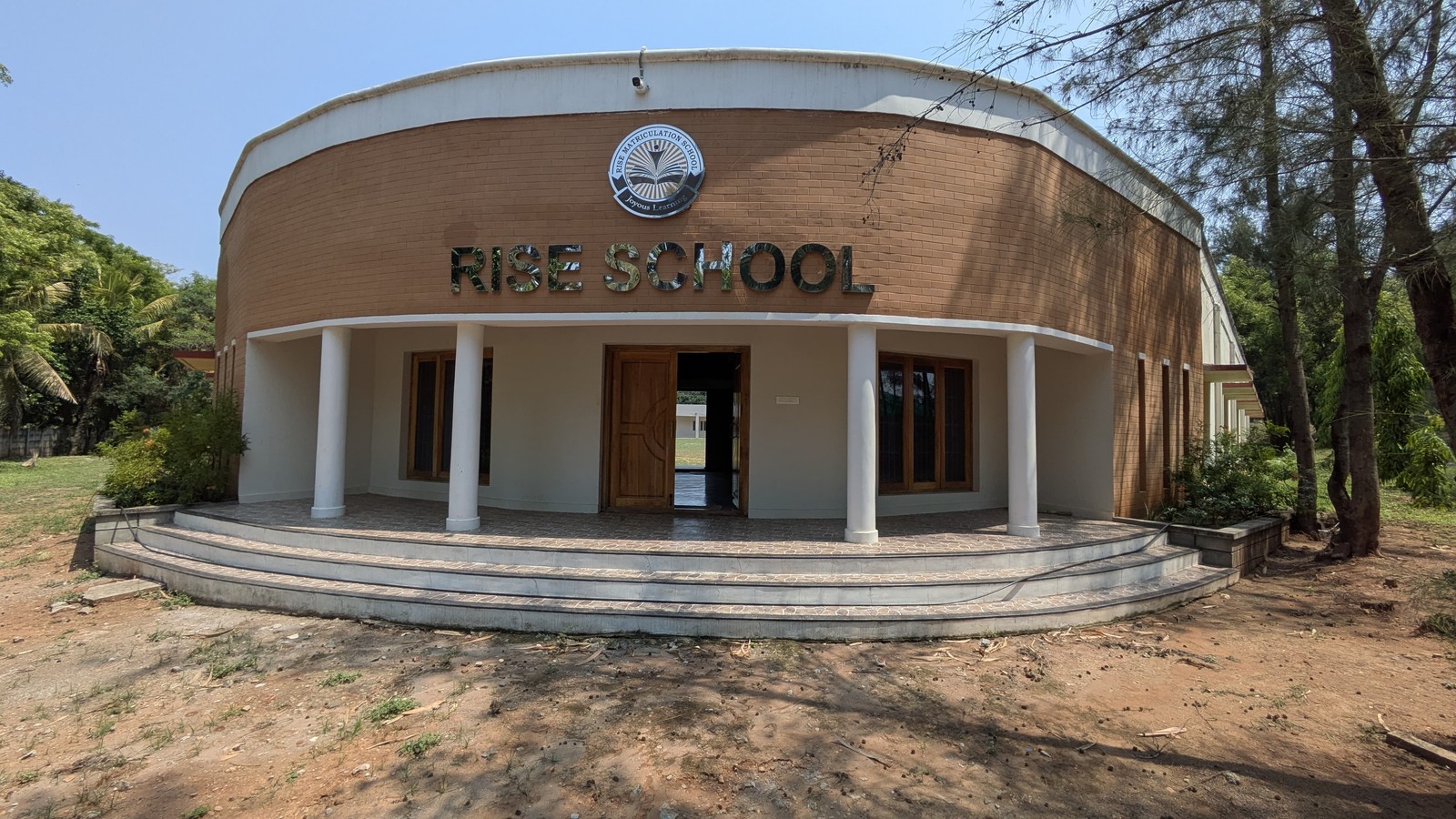 The curved brick front of RISE School with its steel lettering and logo, set among trees